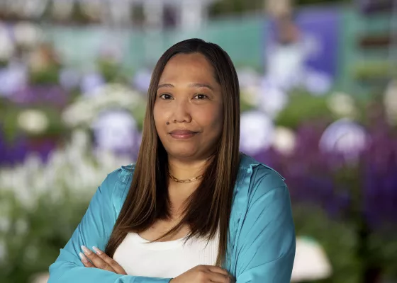 Woman in teal cardigan with arms crossed, blurred flowers in background